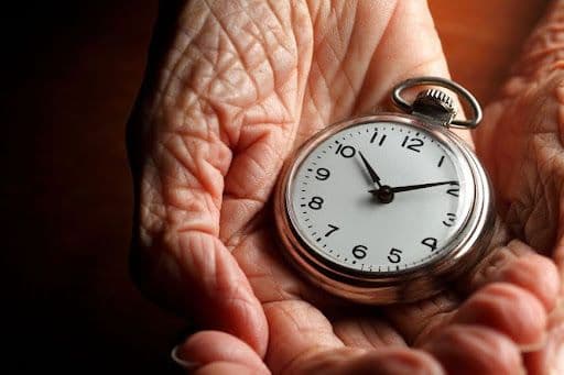 An aged hand holding a hand stopwatch or clock