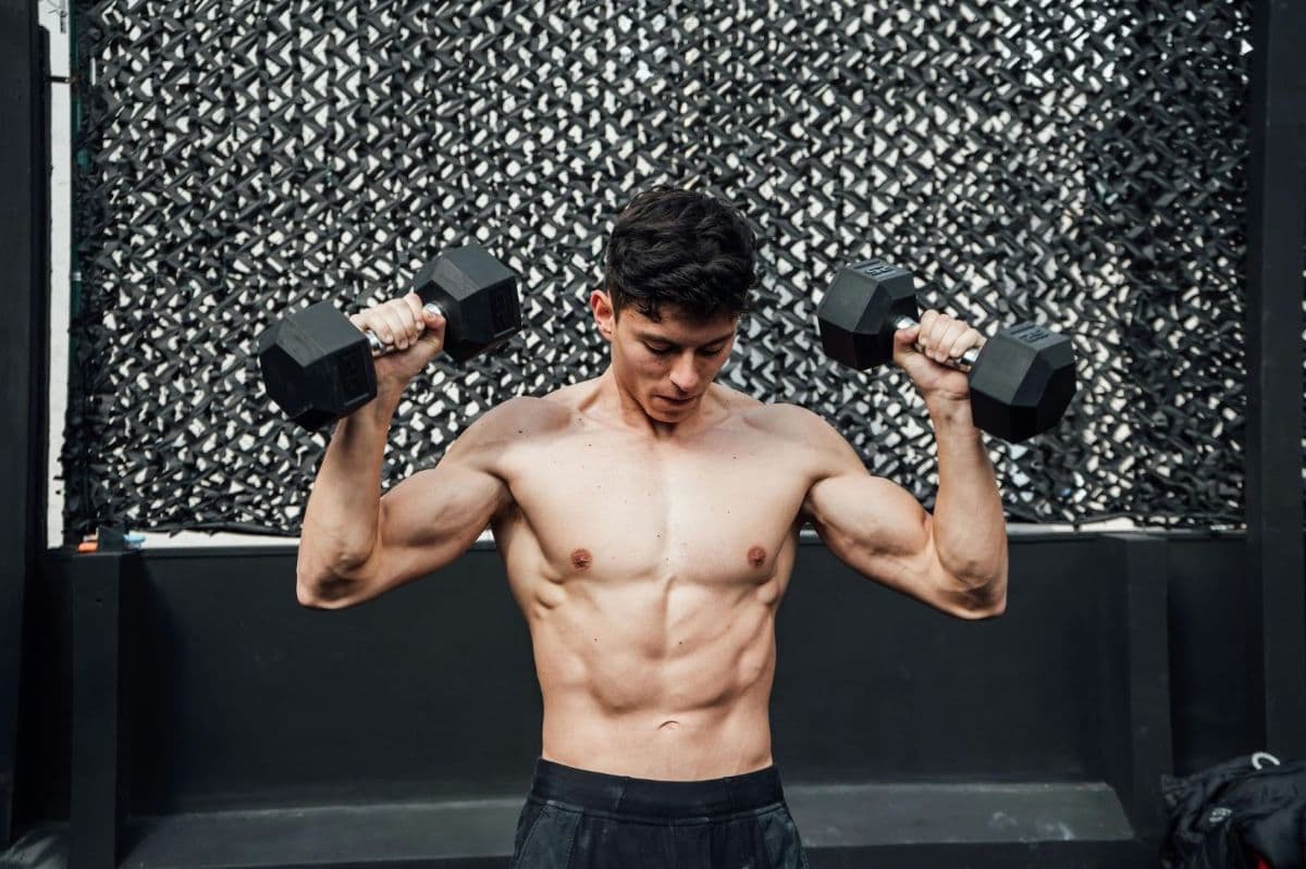 A shirtless man lifting weights in each hand