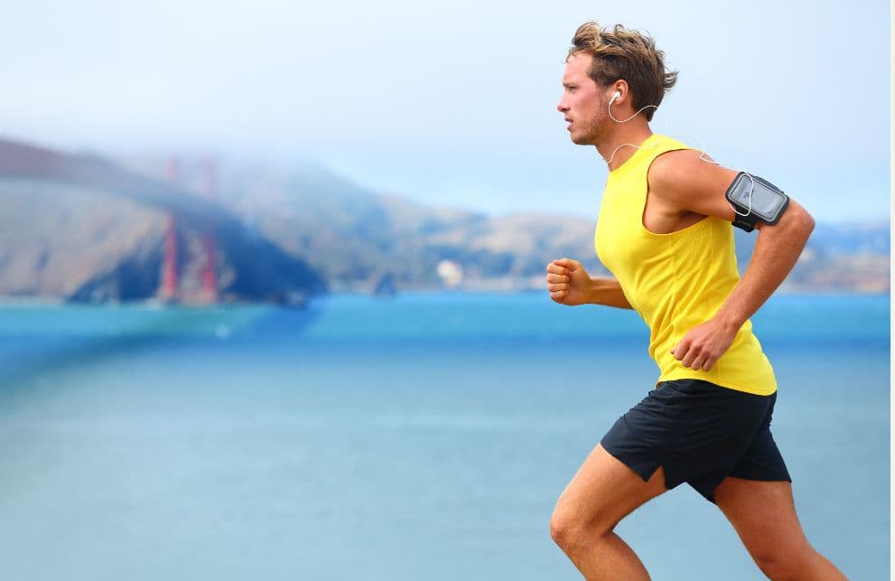 A man running along the beach in San Francisco while wearing a yellow tank top