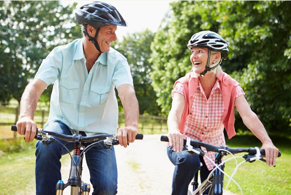 A couple riding their bikes on a trail surrounded by trees and grass