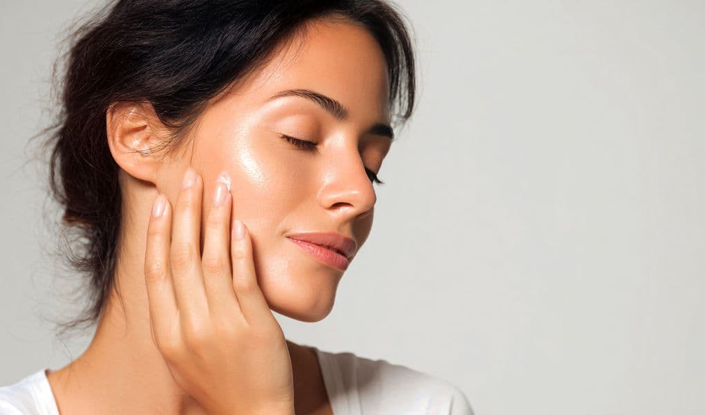 A woman with glowing, youthful, skin caressing her face gently with her hand